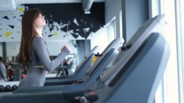 Spor salonundaki koşu bandında gevşek saçlı genç bir kızın yavaş çekim videosu. Sağlıklı vücut kavramı