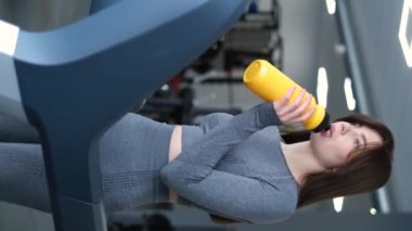 Sarı şişeden su içen ince atletik kızın dikey videosu. Sabah egzersizi. Fitness eğitimi