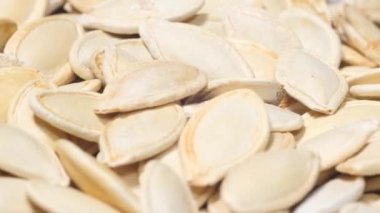 Beyaz bir zeminde dönen beyaz bir tabakta kurumuş kabak tohumlarının video arkaplanı. Diyet vejetaryen yiyecekler. 4k video