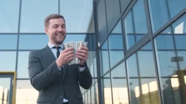 Bir gökdelenin arka planındaki çekici genç bir adam Amerikan dolarlarını elinde tutuyor. Yüksek maaş, yüksek iş geliri.