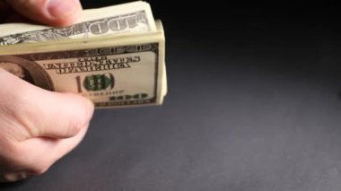 Bir erkek eli dolar banknotlarını tutar ve onları siyah arka planda sayar. Finansal harcamalar, alımlar, birikim. 4k yakın video