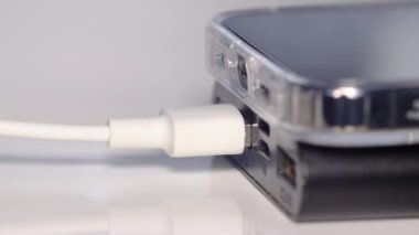 Güç bankasının bataryası beyaz arka planda USB kablosuyla akıllı telefonu şarj ediyor. Modern aletleri yüklemek, seçici odaklanma. 4k video