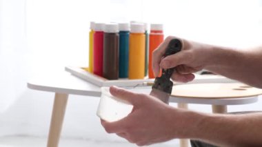 Kapatın. Ressamların eli, kaptaki beyaz boyayı spatulayla karıştırır. Beyaz tonlarda yaratıcı atölye çalışması. Bir resim yaratma süreci. Fırça hareketi