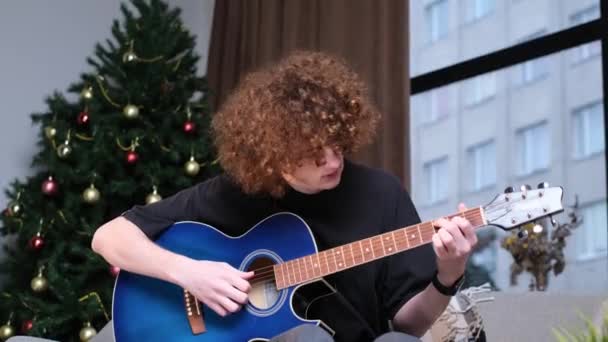 フル長いですポートレートのカジュアル男ともに巻き毛再生ギターに対してクリスマスツリー背景 — ストック動画