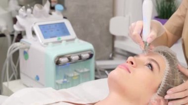 Beautiful woman in a spa salon for cosmetic procedures for facial care. A cosmetologist performs a therapeutic procedure on the face with pulses of low-frequency current in order to prevent the