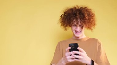 Stüdyoda sarı bir arka planda izole edilmiş akıllı telefonlu şık kızıl saçlı bir genç. Elinde bir aletle genç bir adamın neşeli duyguları. 4k video