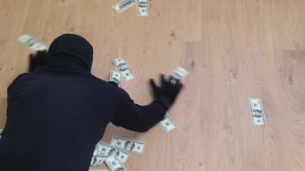 一个穿着黑色巴拉克拉瓦的男人从地板上拿起美元钞票 强盗对被抢的钱很满意 — 图库视频影像