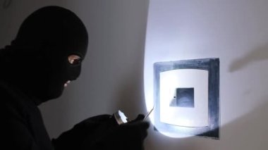 A man in a black mask breaks into a bank vault and opens a safe. A robber steals money from a safe. Bank savings are at risk