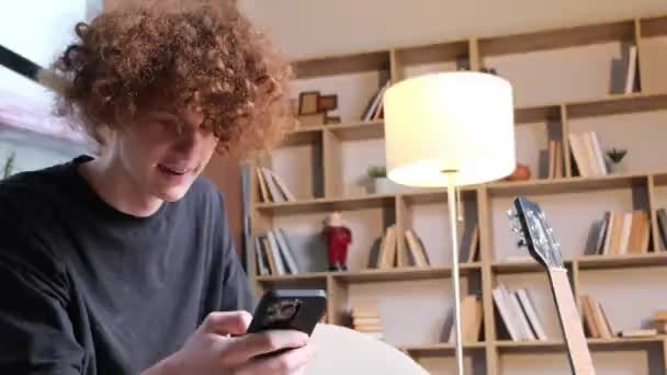 Young Guy Red Hair Sitting Sofa Happy Looking Smartphone Concept — Vídeo de stock