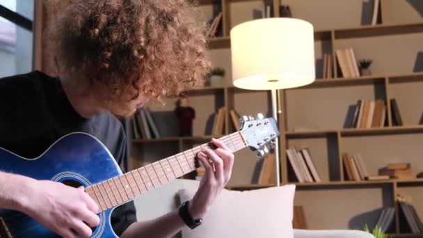年轻时髦的家伙坐在沙发上弹奏吉他 学习弹奏声吉他 — 图库视频影像