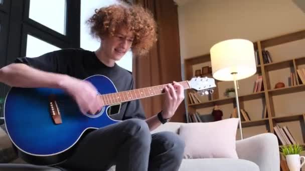 Guy Curly Hair Plays Acoustic Guitar While Sitting Sofa — Vídeo de stock