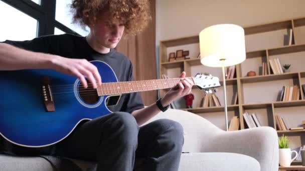 Curly Haired Guy Sitting Sofa Playing Acoustic Guitar Has Headache — Vídeo de stock