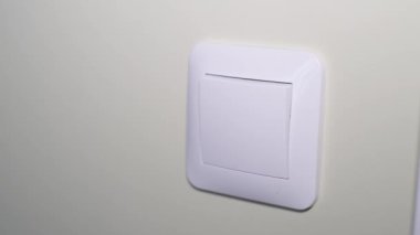 Close-up of a light switch on the wall being turned on by a womans hand. Turning on the lighting in the house. High quality 4k video