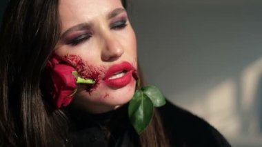 Close-up of a girl with a beautiful makeup artist with a rose in her mouth. Unusual makeup on the face.