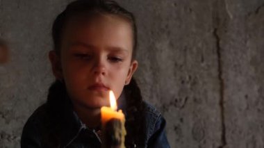 A small child sits in the basement with a candle, rocket attacks on Ukrainian cities. Upset child. War in Ukraine. Energy blackout