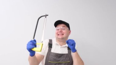 Portrait of a dancing construction worker on a white background, holding a saw for cutting wood. Home renovation concept