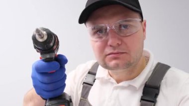 A worker uses an electric drill on a white background in the studio. Repair in the house. 4k video