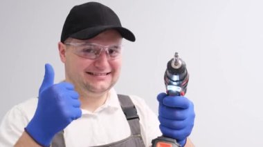 Portrait of a man in a special construction suit and with a drill in his hands, he shows a thumb up. A place to advertise construction