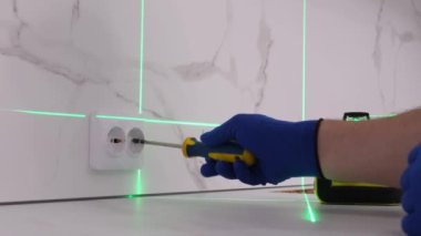 Close-up of an electrician installing a 220 volt outlet, he uses a screwdriver and a level laser. Professional electrician