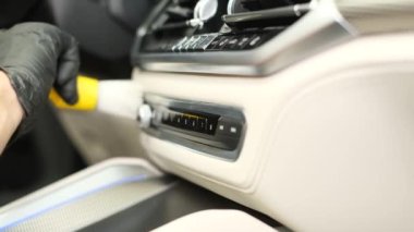 A young employee of a car wash washes the car inside, he wipes the instrument panel with a special brush.