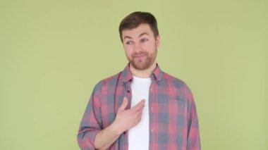 A handsome guy on an olive background flirts, spreads his arms. Emotions of happiness, joy. Good mood. The guy says no, its not me