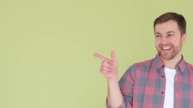 A charming boy in a checkered shirt stands in the studio and points his index finger to the side. Sign language