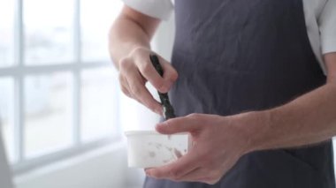 The artist stands and stirs the white paint in the vessel with a spatula. Creative workshop in white tones. The process of creating a picture. Brush movement