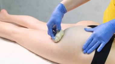 The procedure for removing hair from a womans body. Hands of a female beautician in blue gloves apply cosmetic wax to a clients legs in a modern spa salon.