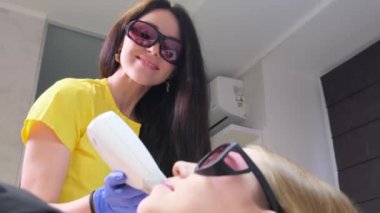 A doctor in gloves removes facial hair from a woman using a modern laser. Epilation for smooth skin, laser procedure. Advertising for a beauty salon