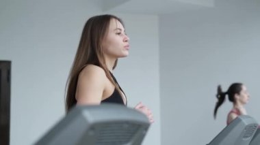 Beautiful girls doing cardio. Two active girls in sportswear work out on a treadmill in the fitness center. The concept of endurance and motivation.