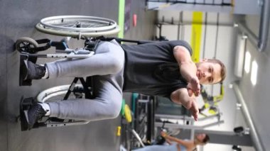 A young determined man with a disability is doing arm exercises in the gym. Warming up before training. Rehabilitation of the disabled. Vertical video.