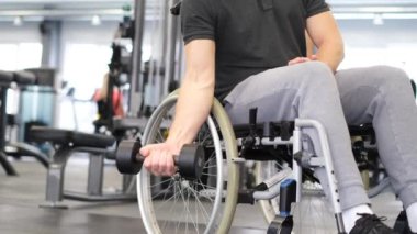 A disabled person in a wheelchair lifts a dumbbell. A person with limited mobility in the gym. Persistent invalid