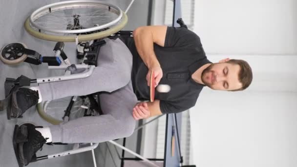 垂直ビデオ 車椅子の若者がラケットとピンポンボールで遊んでいる 障害者はゲームの準備をしている パラリンピアン — ストック動画