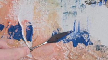 The hand of a talented artist paints an abstract painting on a canvas with a spatula. Contemporary arts