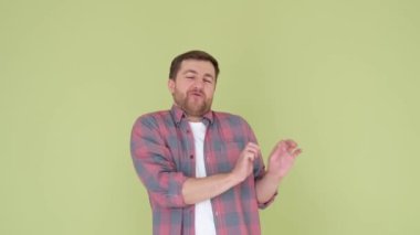 An attractive young man in a colored shirt makes rhythmic movements with both hands. Dancing to the camera in the studio