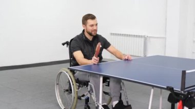 A handsome young bearded man in a wheelchair is playing ping pong. Sports as a hobby and health benefits