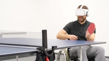 An adult man with a disability wearing virtual reality glasses plays table tennis in a bright hall. The concept of the future