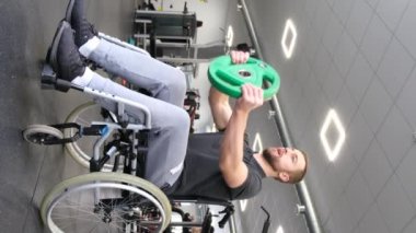 Adult attractive man in a wheelchair works out in the gym, lifting weights, dumbbells. Rehabilitation after injury. Work on your body. Healthy body concept