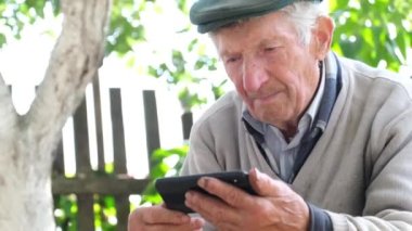 Çok yaşlı, kır saçlı bir büyükbaba akıllı telefonundan bir video izliyor. Eski ve teknoloji