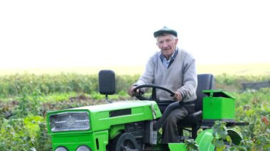 Kendi bahçesinde traktörünün üzerinde oturan pozitif, kendinden emin yaşlı bir çiftçi. Tarlada çalış, bahçe. Sonbahar bir bitki çiftliğinde çalışır. Yaşlı bir çiftçi şapkasını çıkarır ve saçını düzeltir.