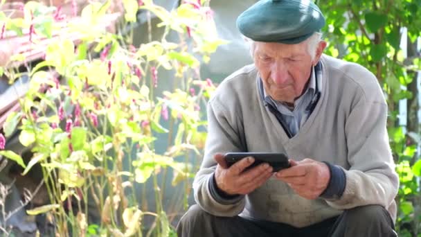 Ein Alter Grauhaariger Großvater Sitzt Zwischen Den Blumen Und Schaut — Stockvideo