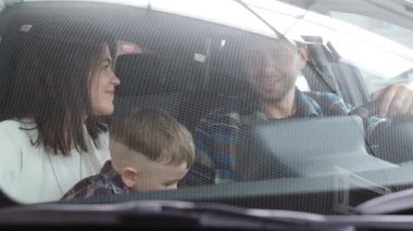 A happy European young couple with a child is testing a new car while sitting in a comfortable car interior. Family shopping.