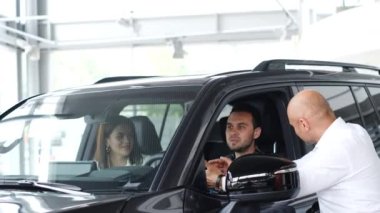 Test drive before buying a car at a car dealership. A sales manager sells a car to a young family. Family car purchase