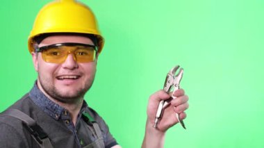 Satisfied, smiling worker with tool on green background in studio. Advertising shooting of a young builder with a European appearance. Thumbs up