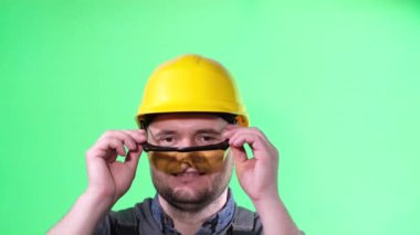 Portrait of a handsome worker in a yellow helmet wearing safety glasses and looking at the camera. Advertising shooting of a builder, locksmith.