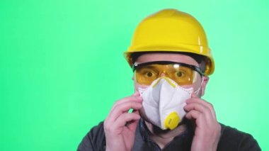 Portrait of a young construction worker in a protective mask, helmet and glasses. Worker on a green background in the studio