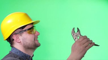 A happy builder on a green background in the studio holds a work tool in his hands. Video shooting of a young builder with an American appearance.