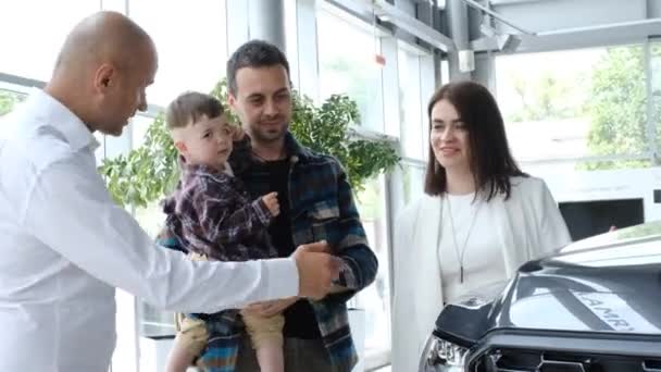 Szczęśliwa Młoda Rodzina Wybiera Nowy Samochód Kierownikiem Salonie Samochodowym Kontrola — Wideo stockowe