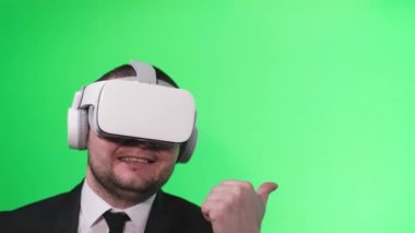 Satisfied smiling man in virtual reality glasses pointing finger at someone. Virtual player. Helmet and glasses