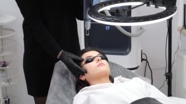 Güzellik salonunda koruyucu gözlüklü genç bir kız. Modern teknolojileri kullanarak lazer yüz kıllarını çıkarma prosedürü